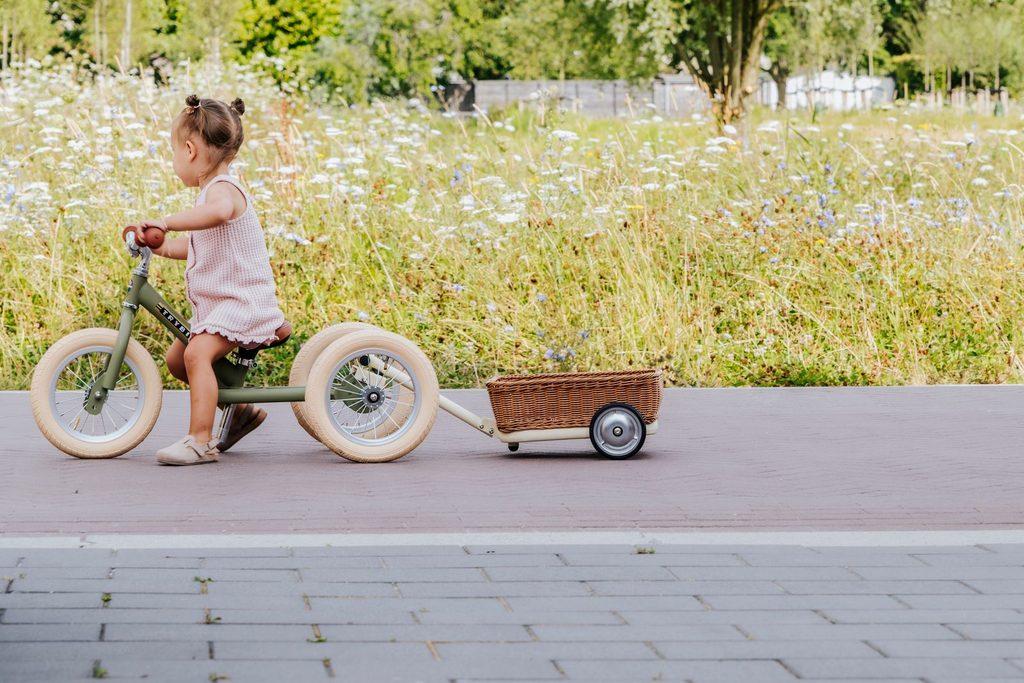 tüdruk sõidab tänaval kolmerattalise jooksurattaga mille taga on Trybike Wagon järelkäru